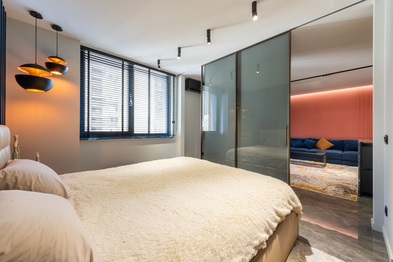 Bed with pillows and cover against glass wall and window in house with lamps in daytime